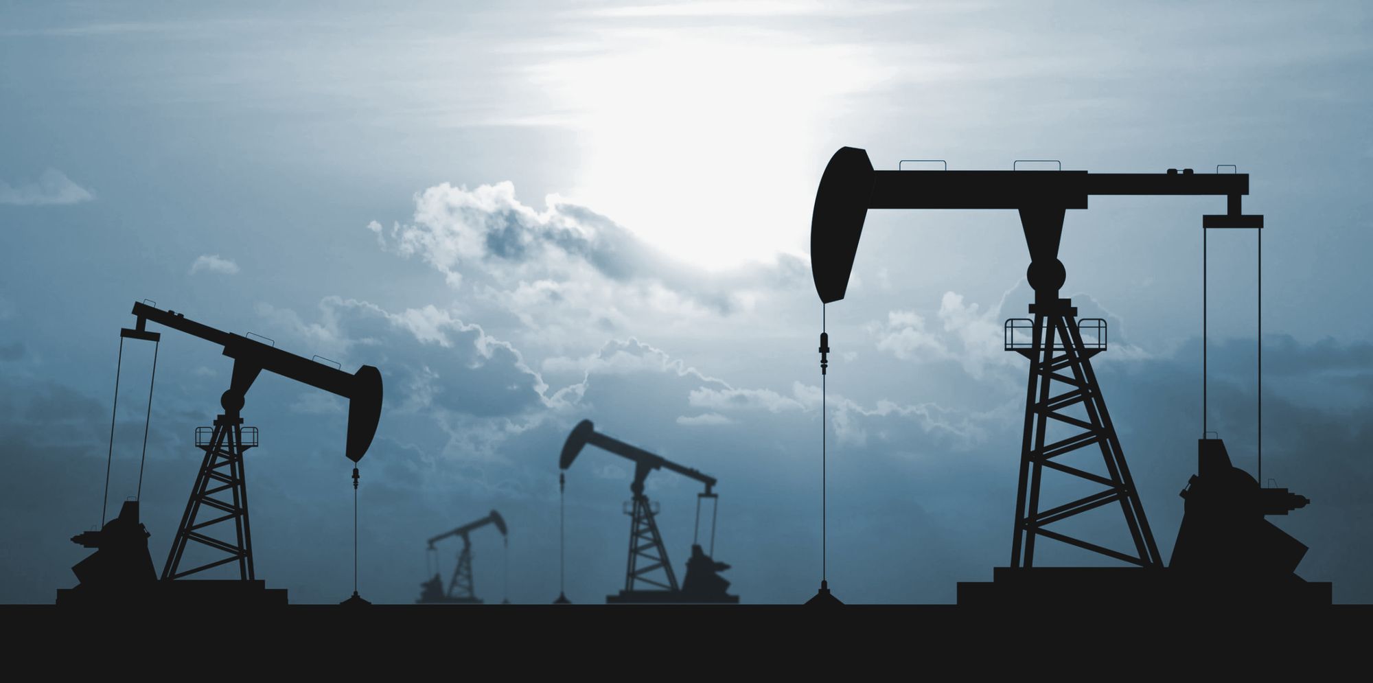 Pumpjacks silhouetted against a cloudy evening sky