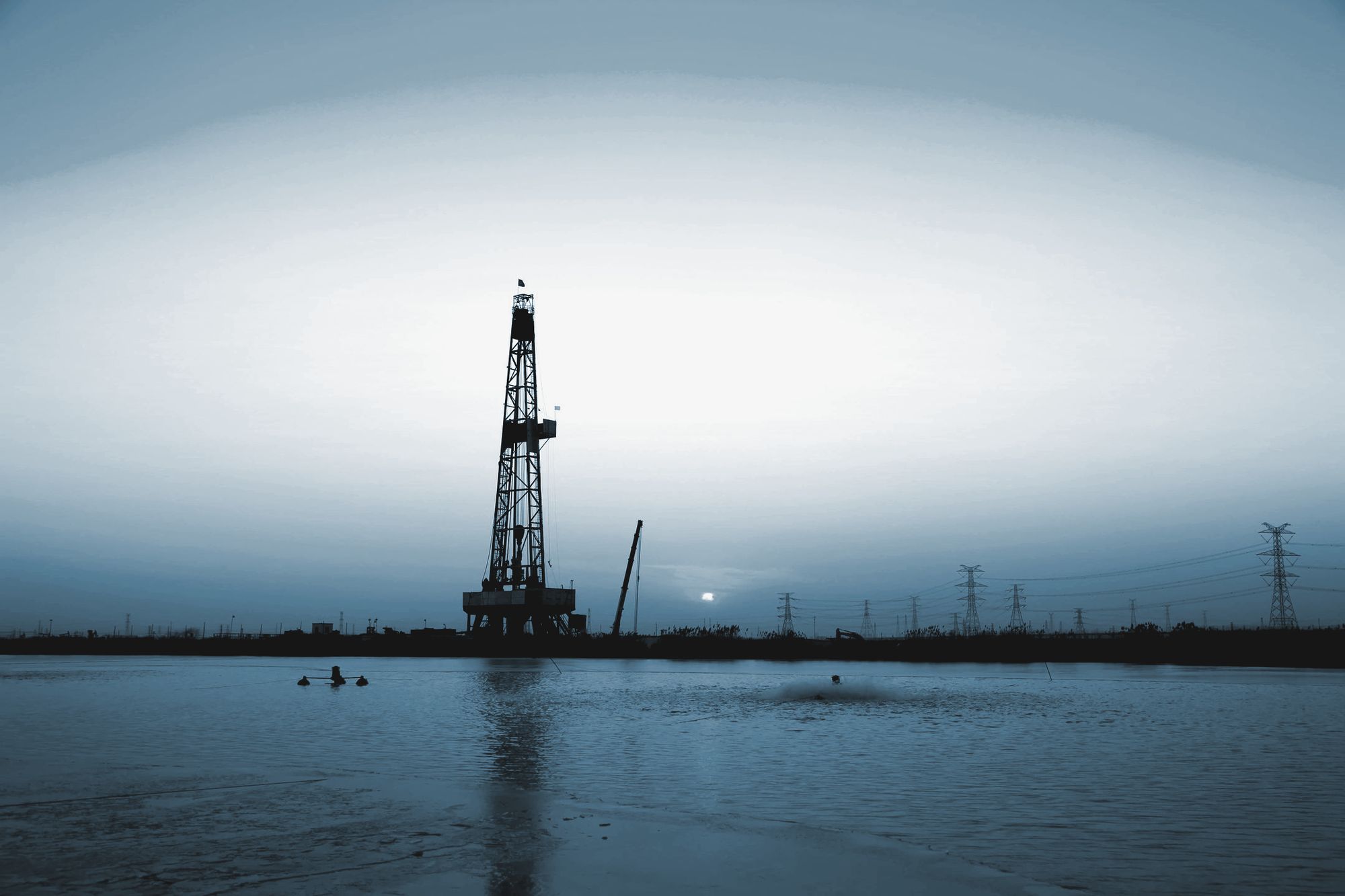 A drilling rig silhouetted at dusk beside open water