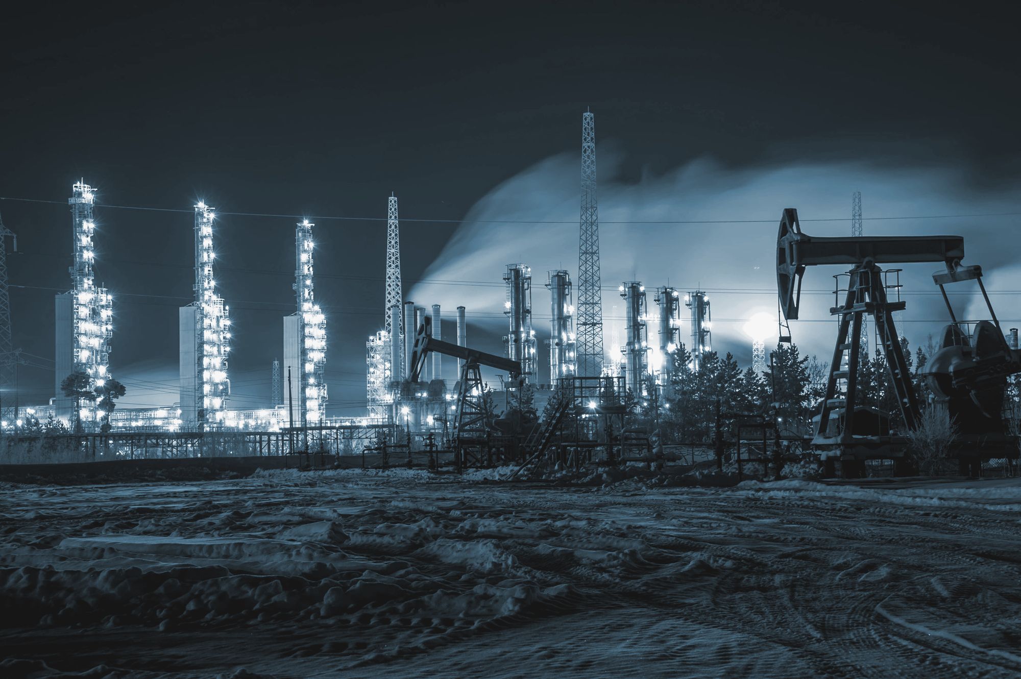A processing plant lit up at night beside a pumpjack